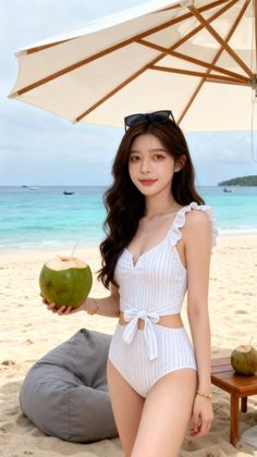Woman in a white striped swimsuit holding a coconut drink on a beach