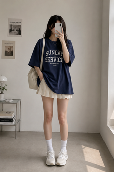 Woman in an oversized t-shirt and pleated skirt taking a mirror selfie