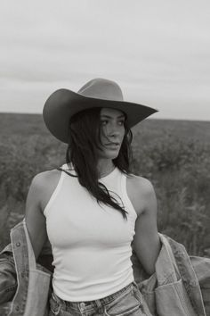 Woman in a cowboy hat and tank top with a denim jacket over her shoulders in a field