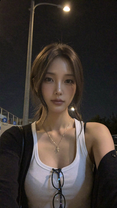 Woman with long hair wearing a white tank top and gold necklace at night