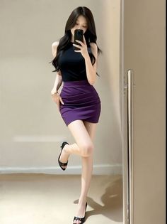 Woman in a black top and purple skirt taking a mirror selfie