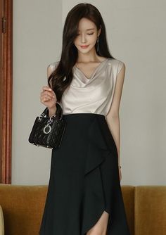 Woman with long hair wearing a draped top and black ruffle skirt, holding a handbag