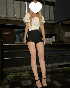 Woman with long blonde hair in a white top and black shorts with sheer pantyhose at night
