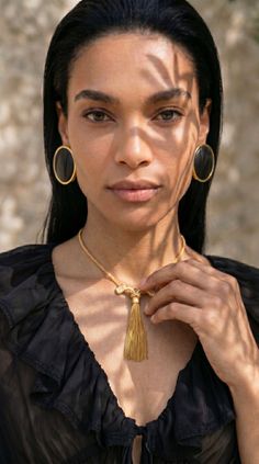 Woman with black hair and gold jewelry in a black ruffled blouse with sunlight and shadows