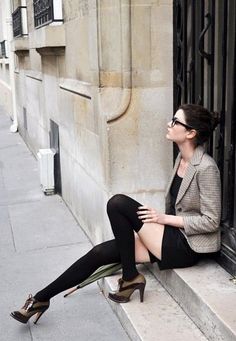 Woman in a black dress and plaid blazer sitting on stone steps outdoors