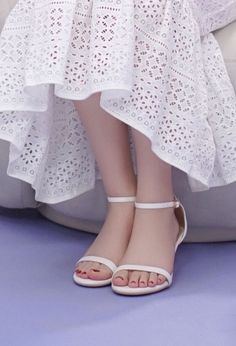 Woman in a white eyelet dress and white sandals with red nail polish