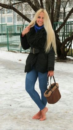 Woman with long blonde hair in a winter coat and jeans standing barefoot in the snow