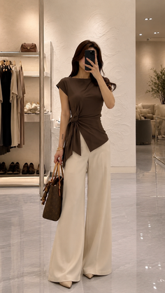 Woman in a brown top and wide leg pants taking a mirror selfie indoors