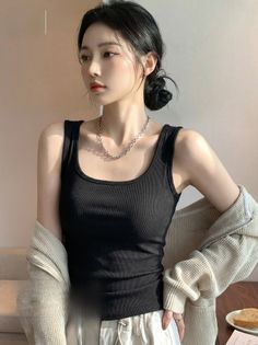 Woman in a black tank top and beige cardigan with hair in a bun