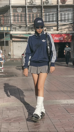 Person in an Adidas jacket, pleated skirt, and leg warmers walking on a street