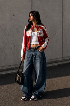 Woman in a red and white racing jacket and baggy jeans outdoors