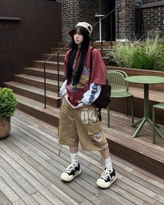 Person with long black hair wearing an oversized t-shirt and cargo shorts outdoors
