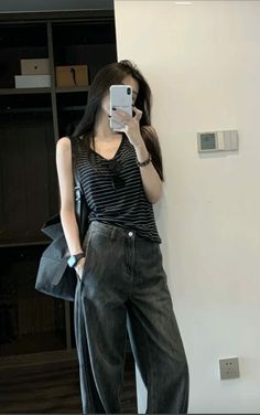 Woman in a striped top and wide leg jeans taking a mirror selfie indoors