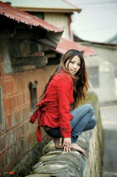 Woman in a red jacket and jeans squatting barefoot on a stone wall