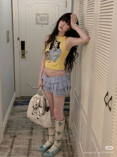 Woman with long hair wearing a yellow crop top and plaid skirt indoors