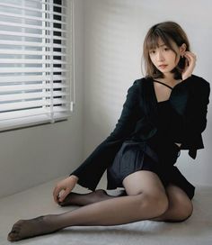 Woman with short hair in a black outfit and pantyhose sitting indoors