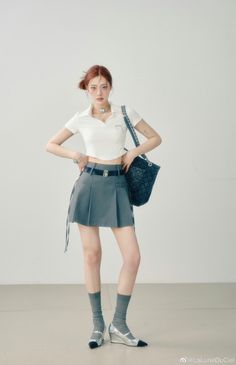 Woman with red hair wearing a cropped top and pleated skirt, posing indoors
