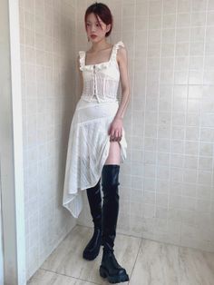 Woman in a white dress and thigh-high boots posing indoors