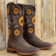 Pair of brown cowboy boots with sunflower embroidery on a wooden surface