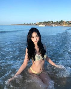Woman in a bikini sitting in the ocean with a beach and palm trees in the background