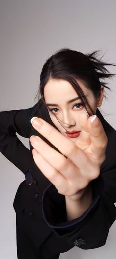 Woman in a black suit with red lipstick and white french tips in a studio shot