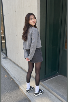 Woman in a denim jacket and skirt with black tights and sneakers outdoors