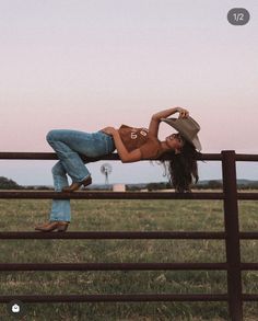 Woman in a cowboy hat and jeans lying on a fence in the countryside at sunset