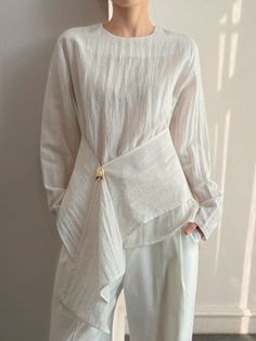 Person in a white long-sleeve blouse with a gold button detail
