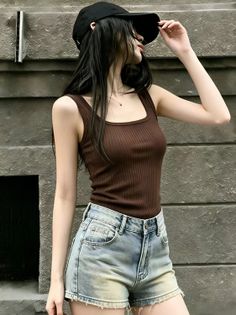 Woman in a brown tank top and denim shorts with a baseball cap outdoors