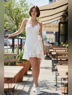 Woman in a white summer dress and sneakers walking past an outdoor cafe