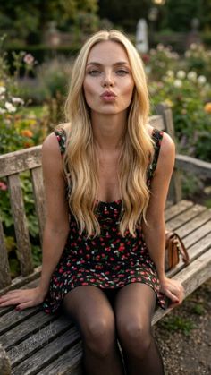 Blonde woman with freckles in a floral dress and black tights sitting on a park bench