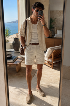 Man in linen shirt and shorts taking a mirror selfie with an ocean view