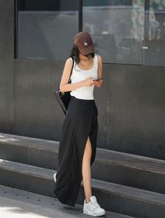 Woman in a white tank top and black skirt with a brown baseball cap walking outdoors