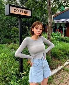 Woman with short hair wearing a long sleeve shirt and denim shorts outdoors