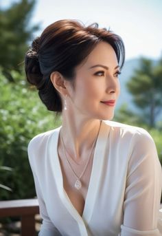 Woman with an updo wearing a white blouse and jewelry outdoors