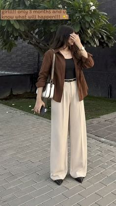 Woman in a brown shirt and wide leg pants holding a phone outdoors