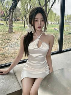 Woman in a white halter neck dress sitting by a window with an outdoor view