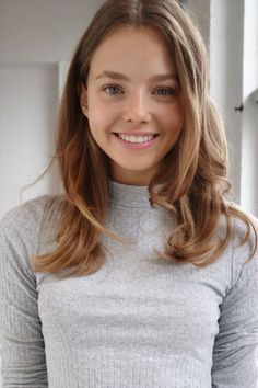 Young woman with long hair and a grey ribbed top smiling at the camera