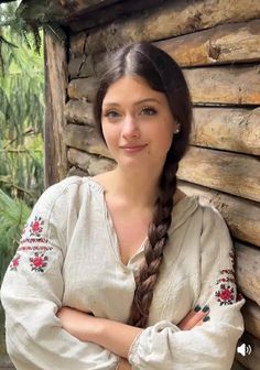 Woman with a long braid and embroidered shirt leaning against a wooden wall