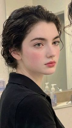 Woman with short dark hair and pink blush in a black shirt indoors