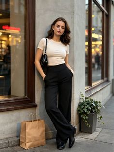 Woman in a crop top and black pants leaning against a building on a street