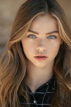 Young person with long hair and blue eyes wearing a plaid shirt
