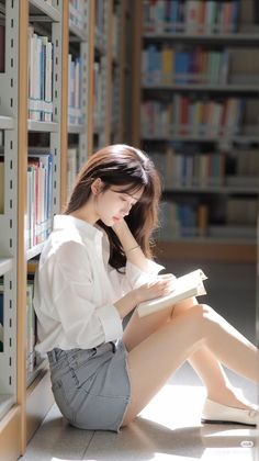 Woman with long hair sitting on the floor in a library, reading a book