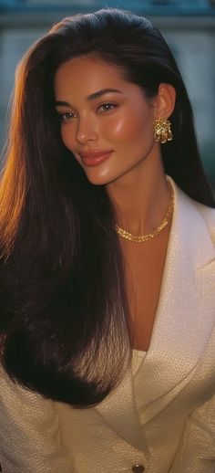 Woman with long dark hair wearing a white blazer and gold jewelry