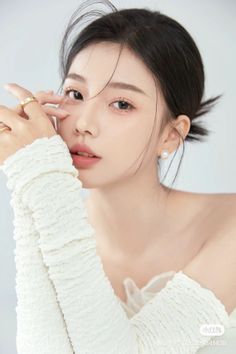 Woman with black hair and pearl earrings wearing a white off-shoulder top