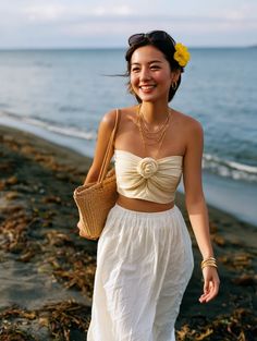 Woman with a yellow flower in her hair walking on a beach with a straw bag