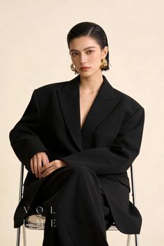 Woman with short hair and gold earrings wearing a black suit in a studio