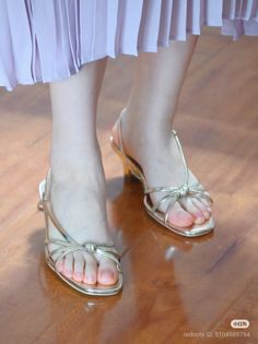Person wearing gold sandals and a light purple pleated skirt on a wooden floor