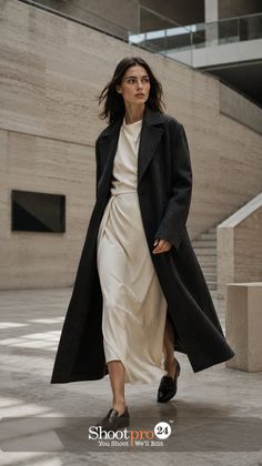 Woman in a long dark coat and cream dress walking indoors