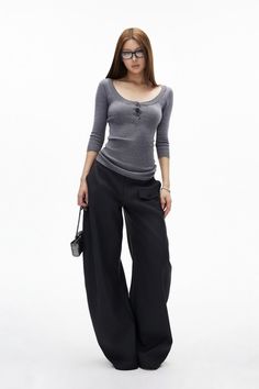 Woman with long hair and glasses wearing a gray top and wide leg pants